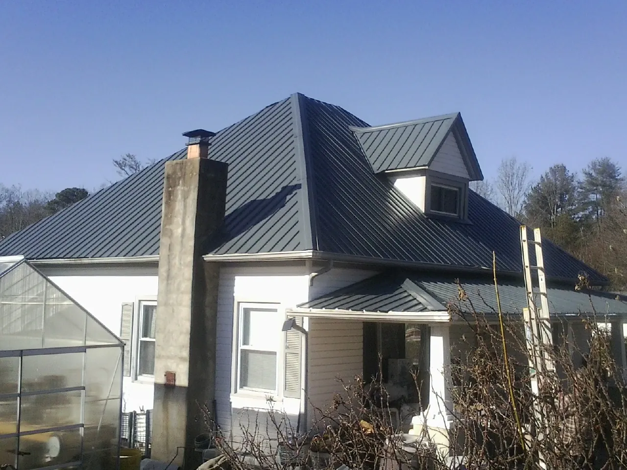 Dark blue standing seam metal roof on a white farmhouse with dormer — Slate & Tile Roof Repair by Roofing Brothers in Menasha