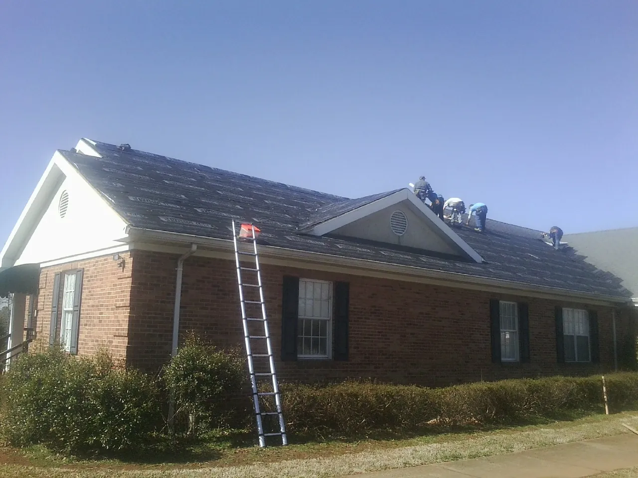 Crew tearing shingles off a brick ranch roof with a ladder set — Metal Roof Repair work by our crew in Menasha