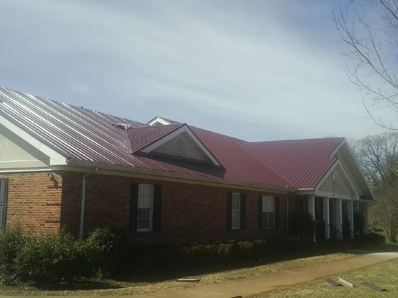 Red metal roof with gabled entries on a long brick building, from a Hail Damage Roof Repair job in Menasha