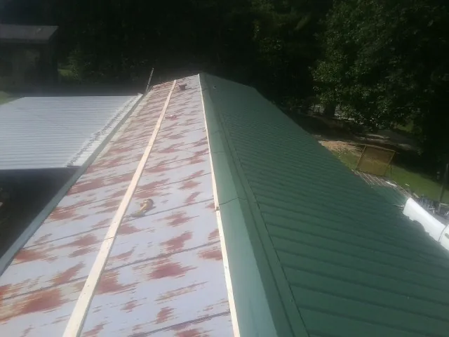 Old rusted panels beside newly installed green metal roofing — Wind Damage Roof Repair by Roofing Brothers in Menasha