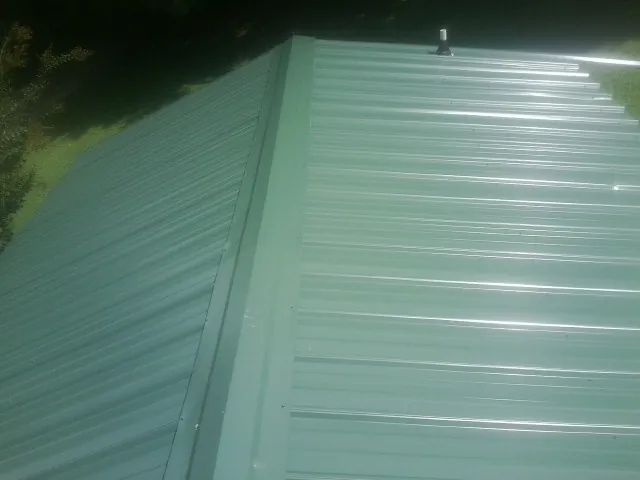 New green metal panels meeting at the ridge of a roof — Flat Roof Repair work by our crew in Menasha