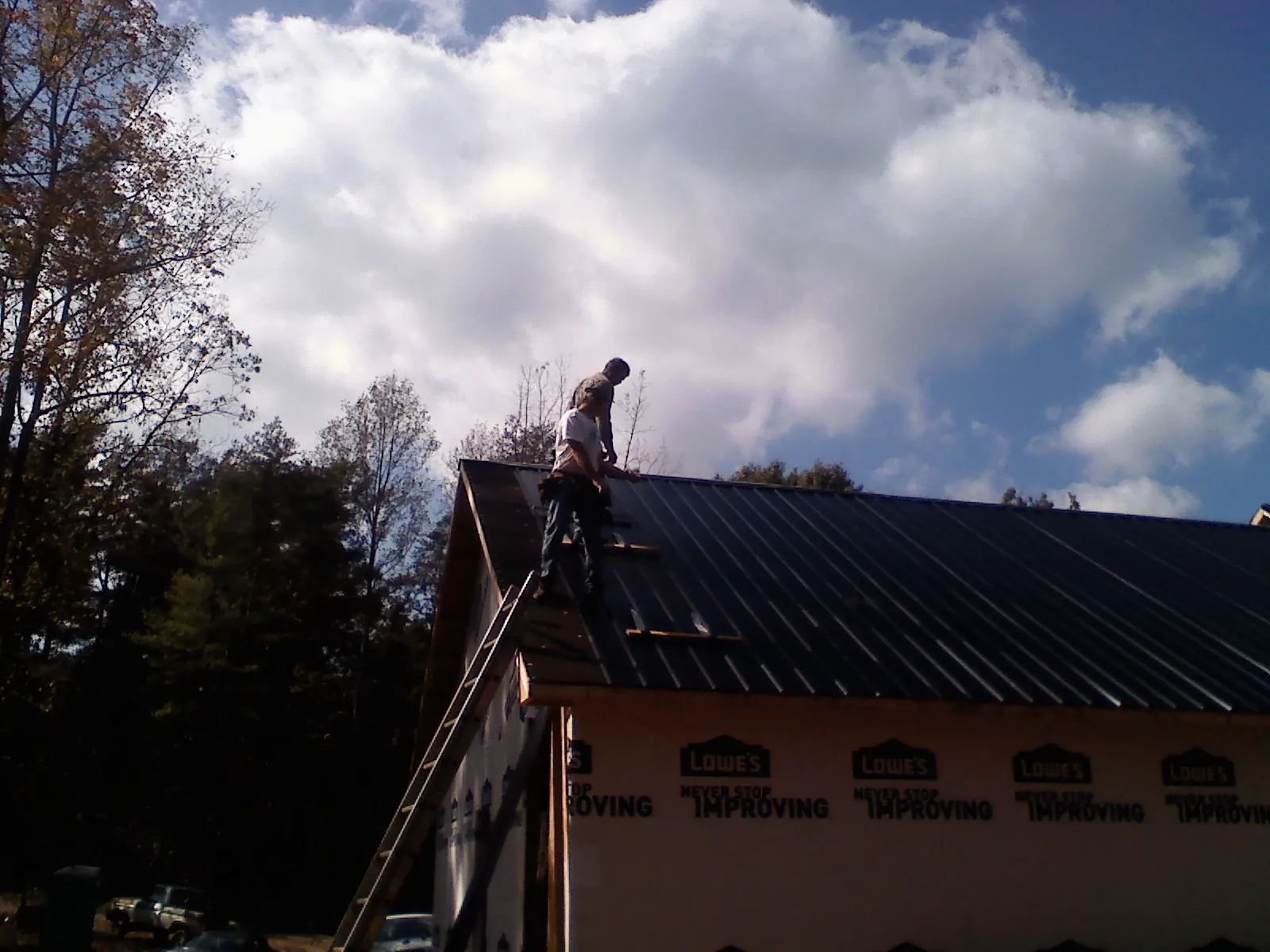 Roofer fastening dark metal panels high against a cloudy sky, from a Roof Inspection job in Menasha