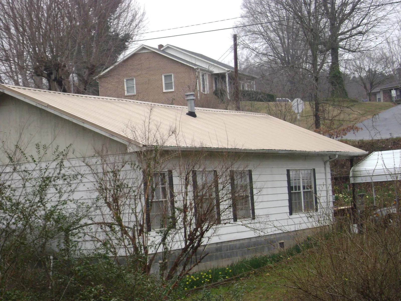 Tan metal roof on a white sided house set into a hillside — Commercial Roofing by Roofing Brothers in Menasha