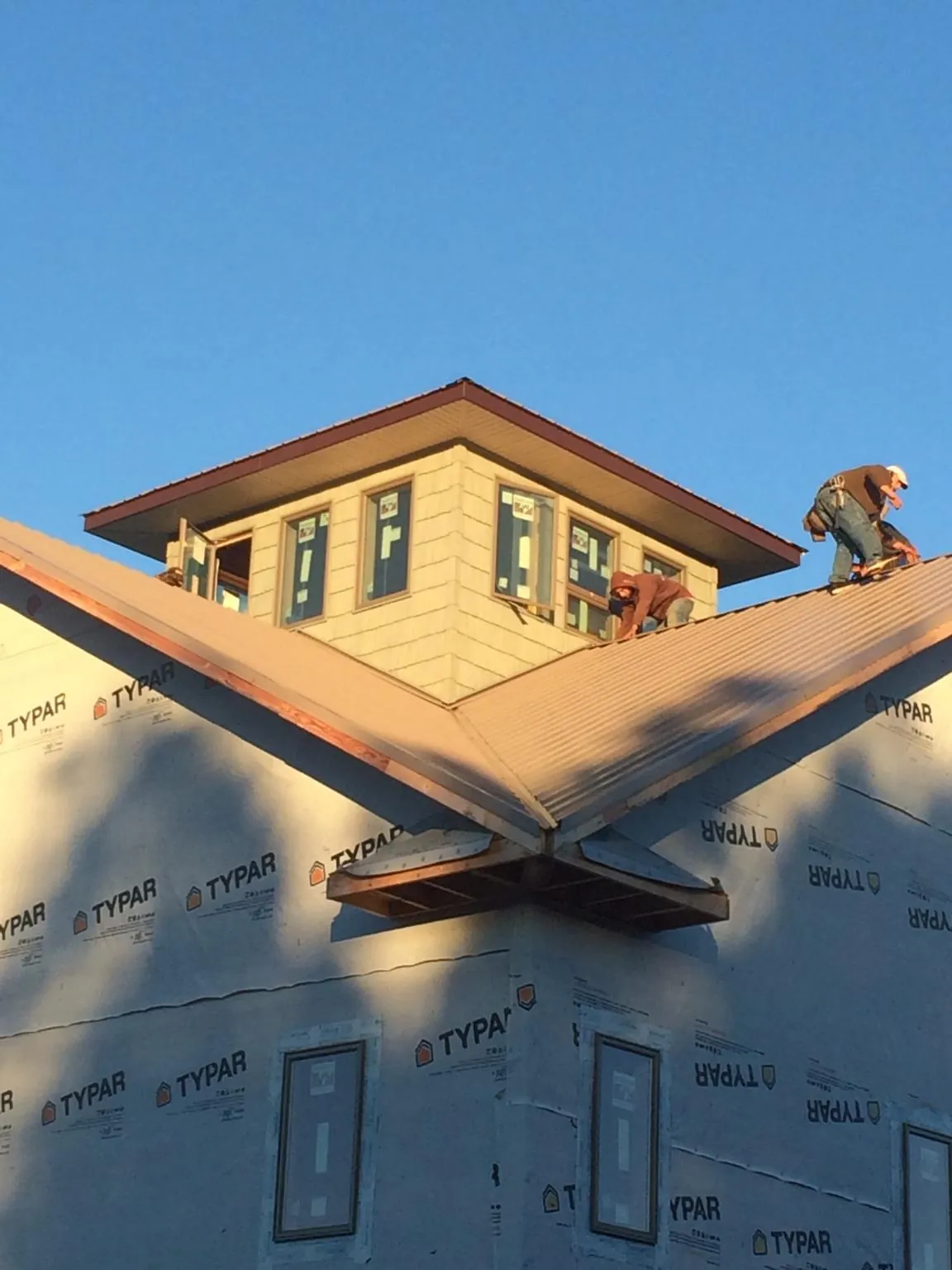Roofers working around a rooftop cupola on a new metal roof at sunset — Roof Waterproofing in Menasha by Roofing Brothers